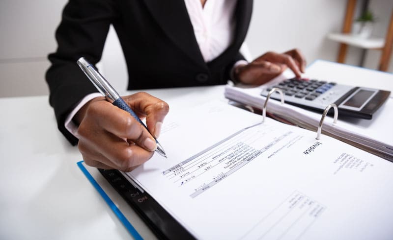 A person writing in a binder with invoices