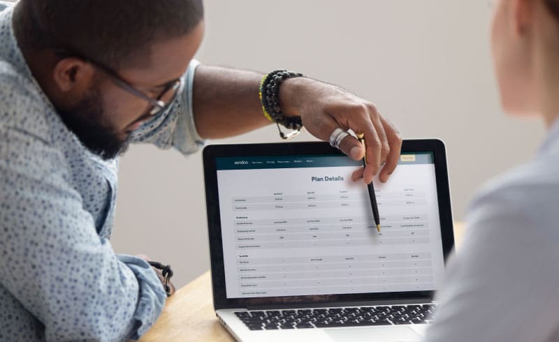 Black male consultant points to a laptop screen with bookkeeping plan details. He is discussing options with a potential customer