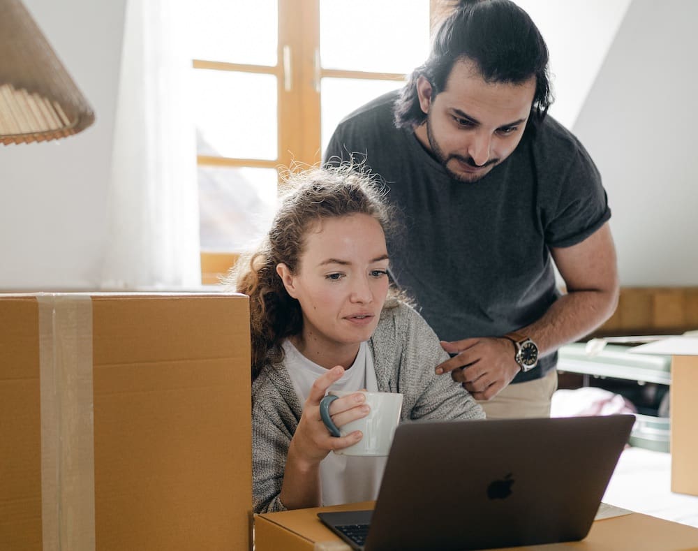 Two people surrounding by boxes look at a computer