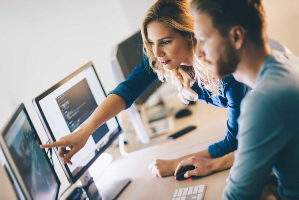 White female business over pointing at a computer and speaking to her white male employee